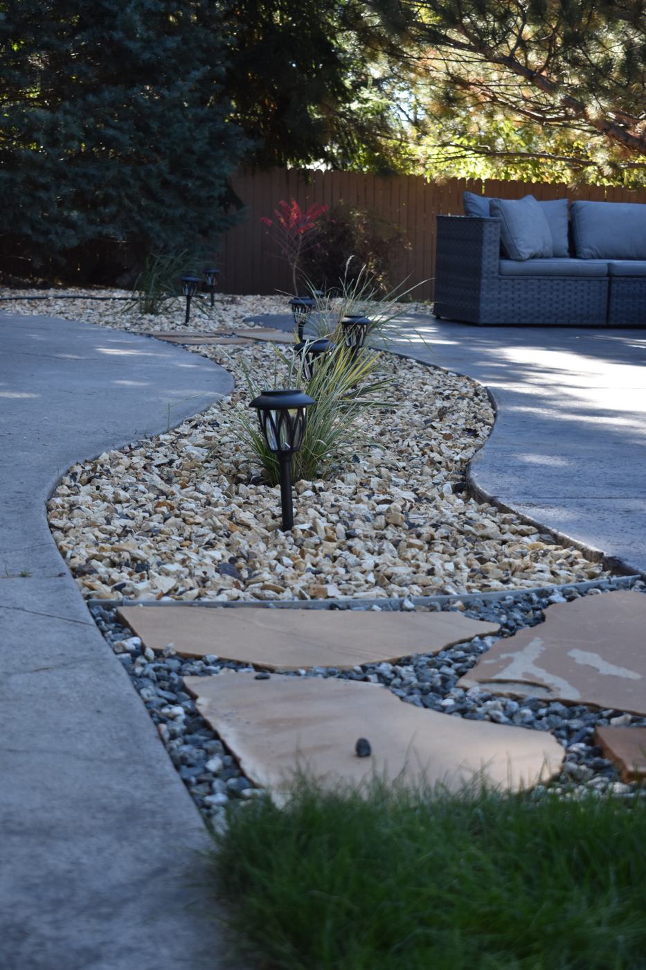 A flagstone path through rock landscaping beds beside a curved concrete walkway.