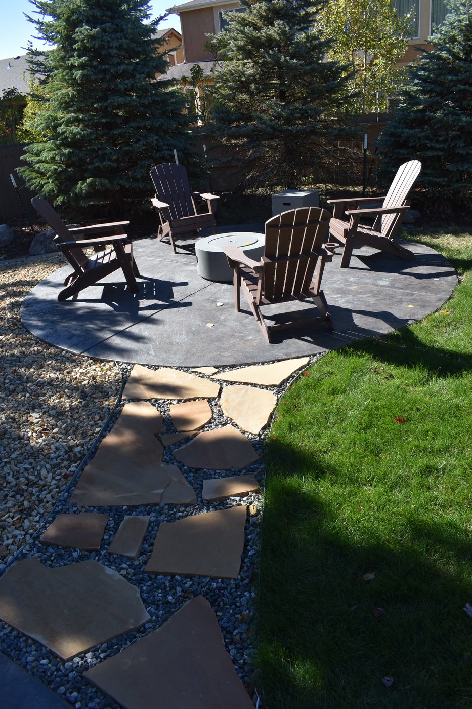 A flagstone path through gravel leading to a fire pit with Adirondack chairs.