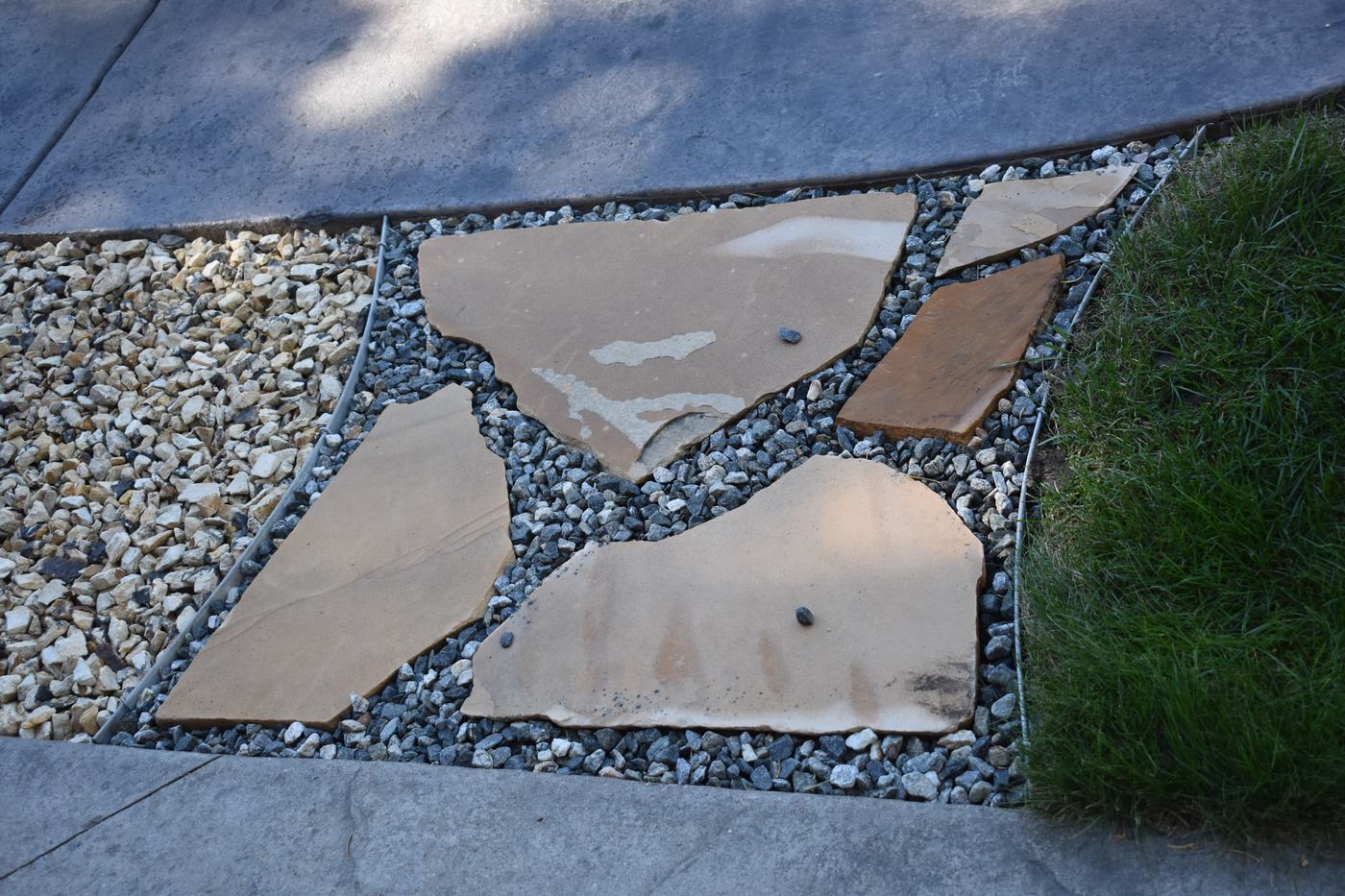 Flagstone stepping stones set in gravel between a concrete patio edge and the lawn.