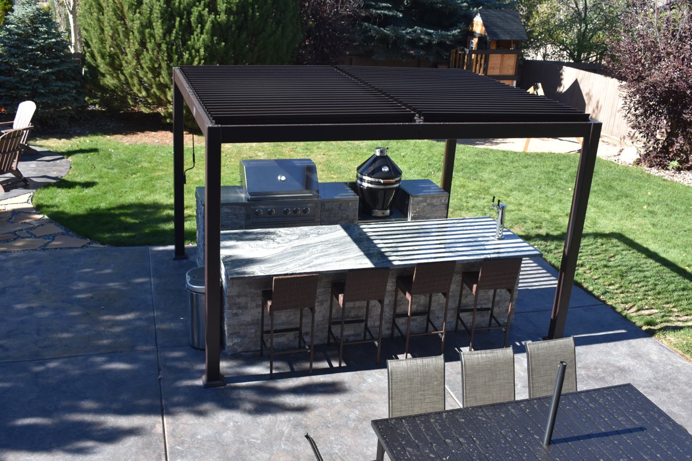 A louvered pergola over an outdoor kitchen and bar on a stamped concrete patio.