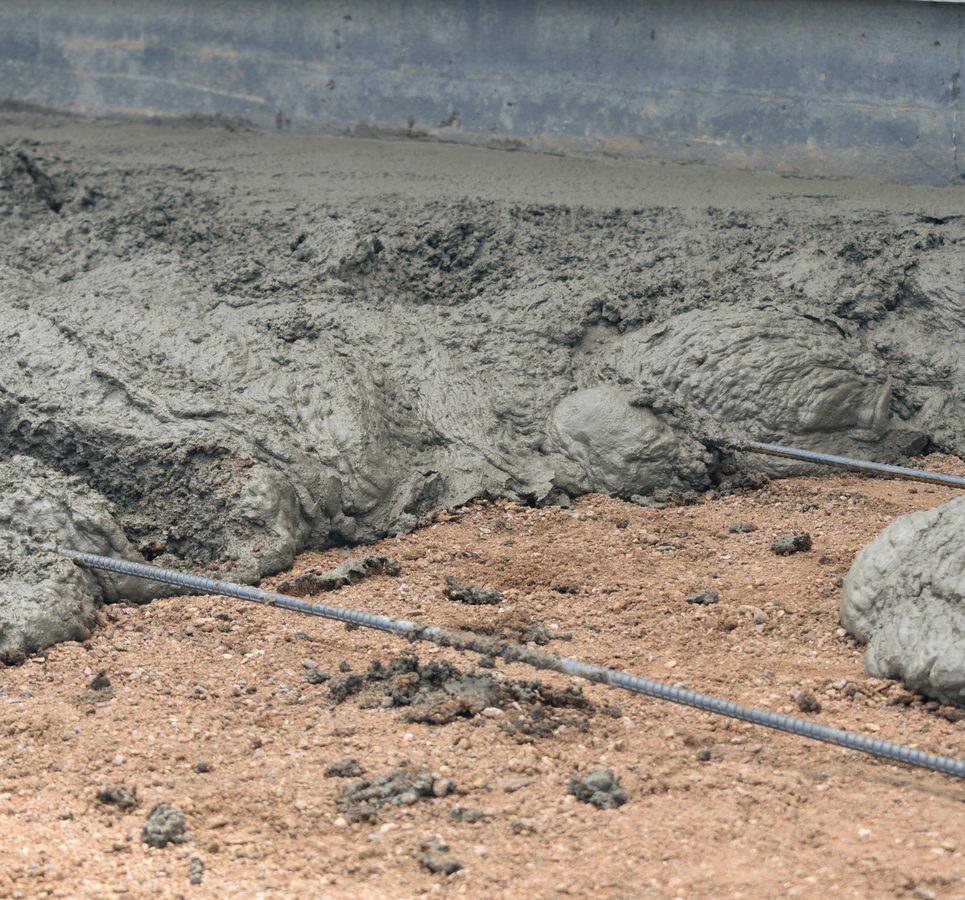 Wet concrete being poured over a #4 rebar grid set on a compacted gravel base.